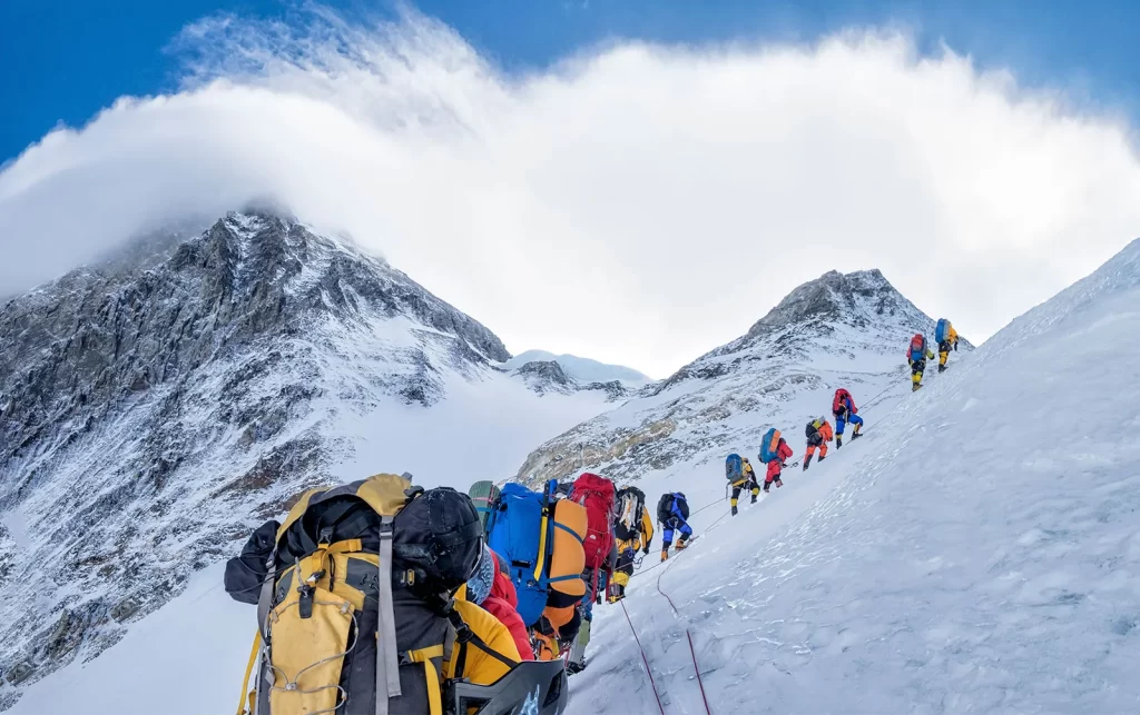 Climbers ascending a steep snow-covered slope near the summit of Mount Everest in Nepal, showcasing the challenges of high-altitude mountaineering and the need for new permit regulations.